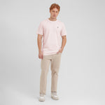 Man wearing a light pink t-shirt and beige pants on a white background