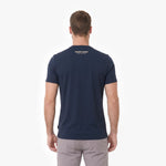 A man viewed from behind, wearing a navy blue T-shirt with 'JAMES BARK' printed in gold on the upper back