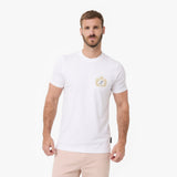 A man wearing a white T-shirt with a small gold and blue crest logo on the left chest