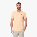 A man wearing a light peach-colored short-sleeve polo shirt with a small embroidered logo on the left chest.