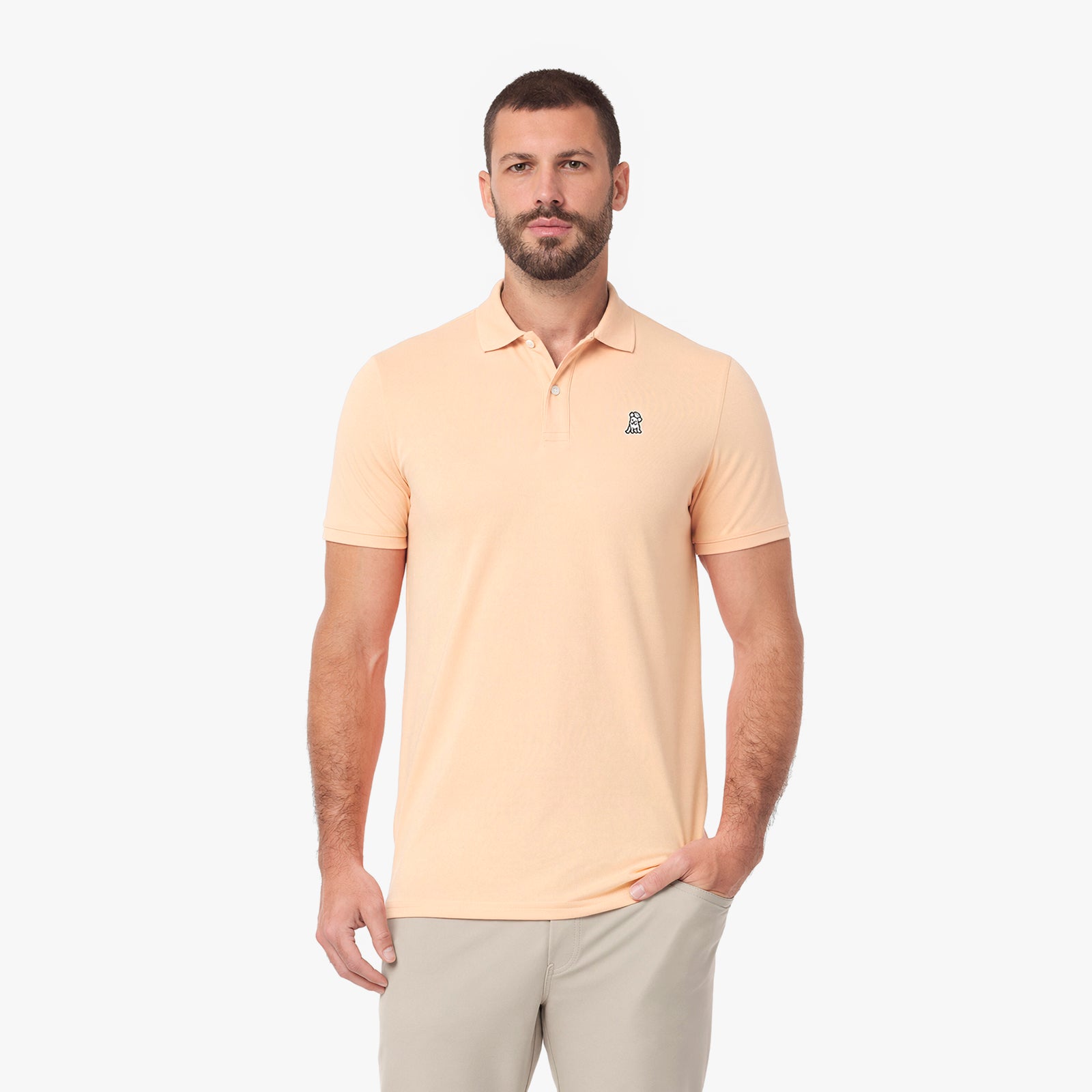 A man wearing a light peach-colored short-sleeve polo shirt with a small embroidered logo on the left chest.
