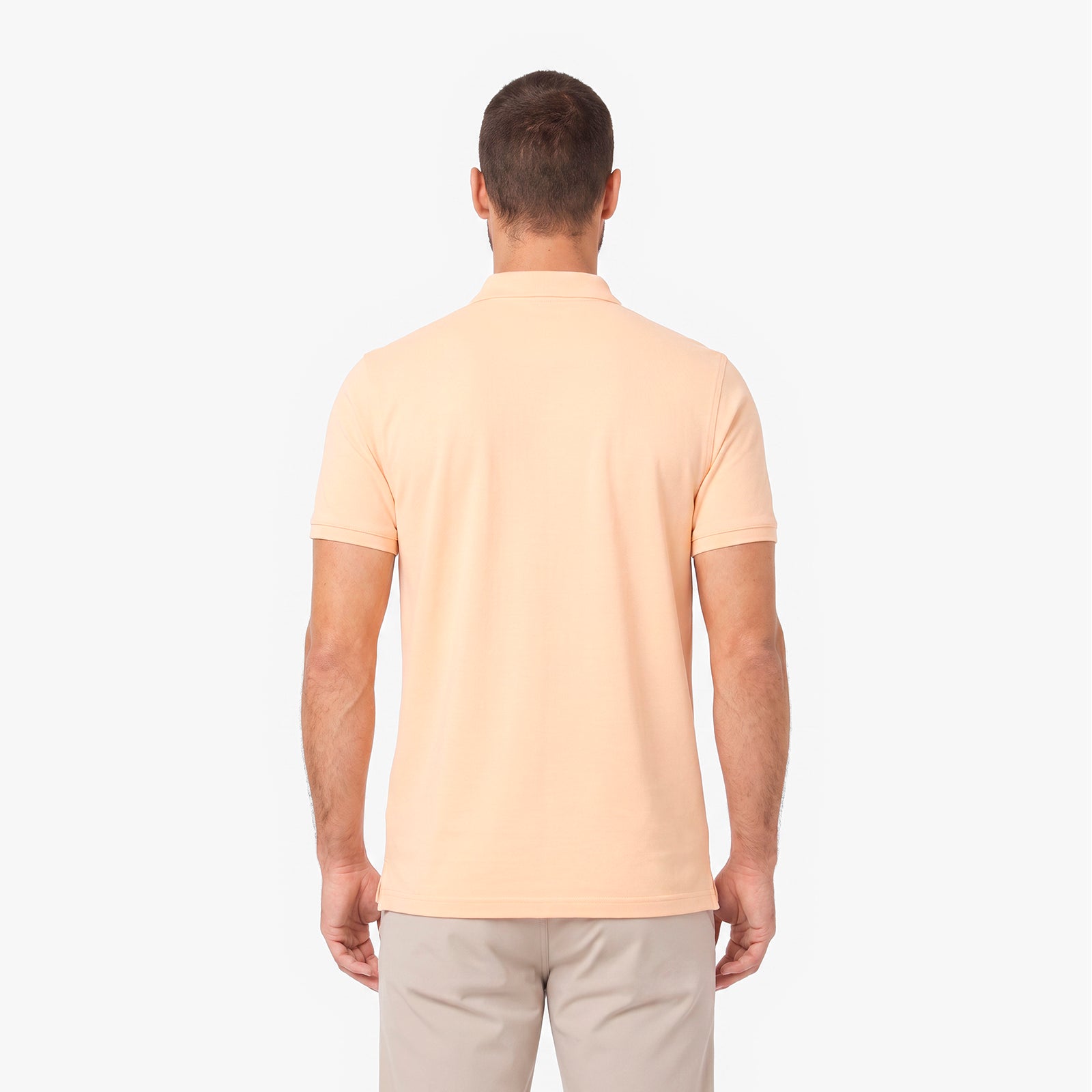 A man viewed from the back wearing a light peach-colored short-sleeve polo shirt.