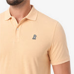A close-up of a man wearing a light beige polo shirt with a small embroidered dog logo on the chest.