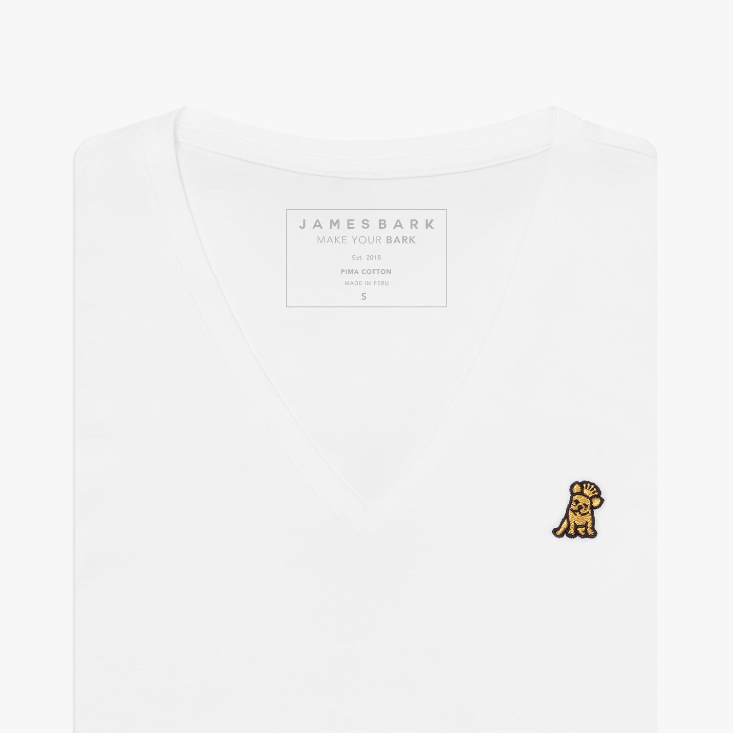 Close-up of a folded white v-neck t-shirt, showing the printed inner neck label "JAMES BARK, MAKE YOUR BARK, PIMA COTTON, MADE IN PERU, S" and a small yellow and black embroidered dog logo on the left chest
