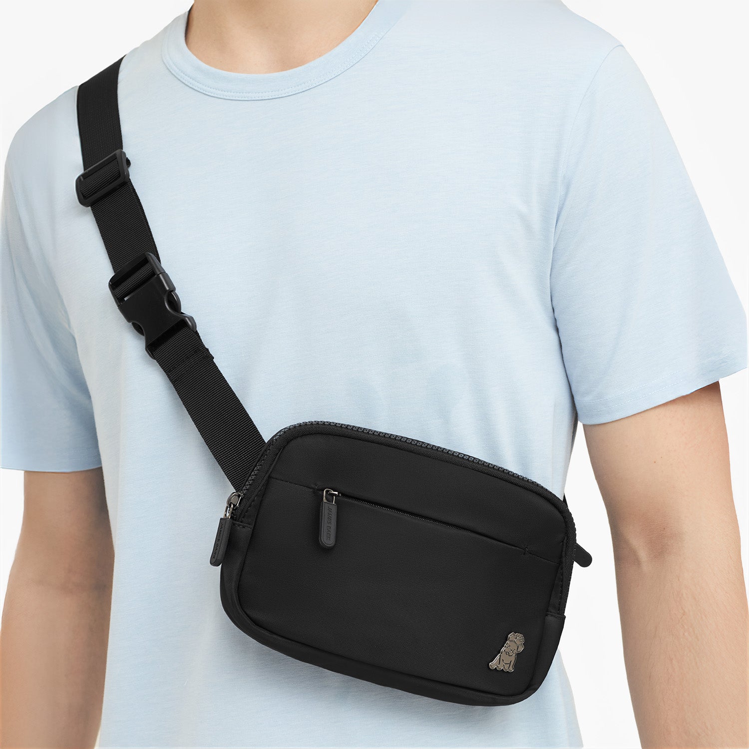 Person wearing a black crossbody bag on a plain background