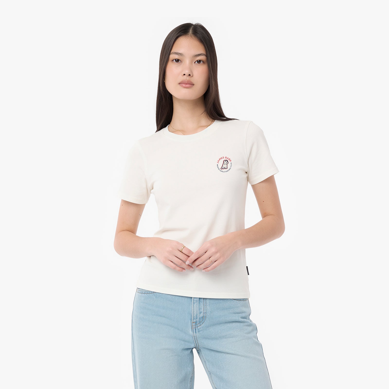 A woman modeling a T-shirt in off-white, featuring a small circular graphic on the left chest, paired with light blue jeans