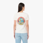 A woman viewed from the back wearing a cream-colored T-shirt with a large colorful 'James Bark Sailing Club' graphic on the back, paired with light blue jeans
