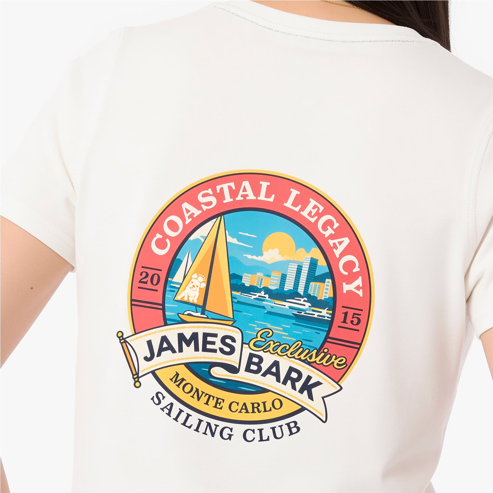 A close-up of a person wearing a white T-shirt, showing the back of the shirt with a large colorful graphic print. The graphic features a sailboat on blue water with a city skyline in the background, enclosed in a red circular border