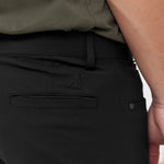 Close-up of black pants with a brand logo on a neutral background