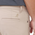 Close-up of beige pants with a brand logo on the pocket against a white background