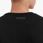 Close-up of a black t-shirt with a brand label on the collar against a white background