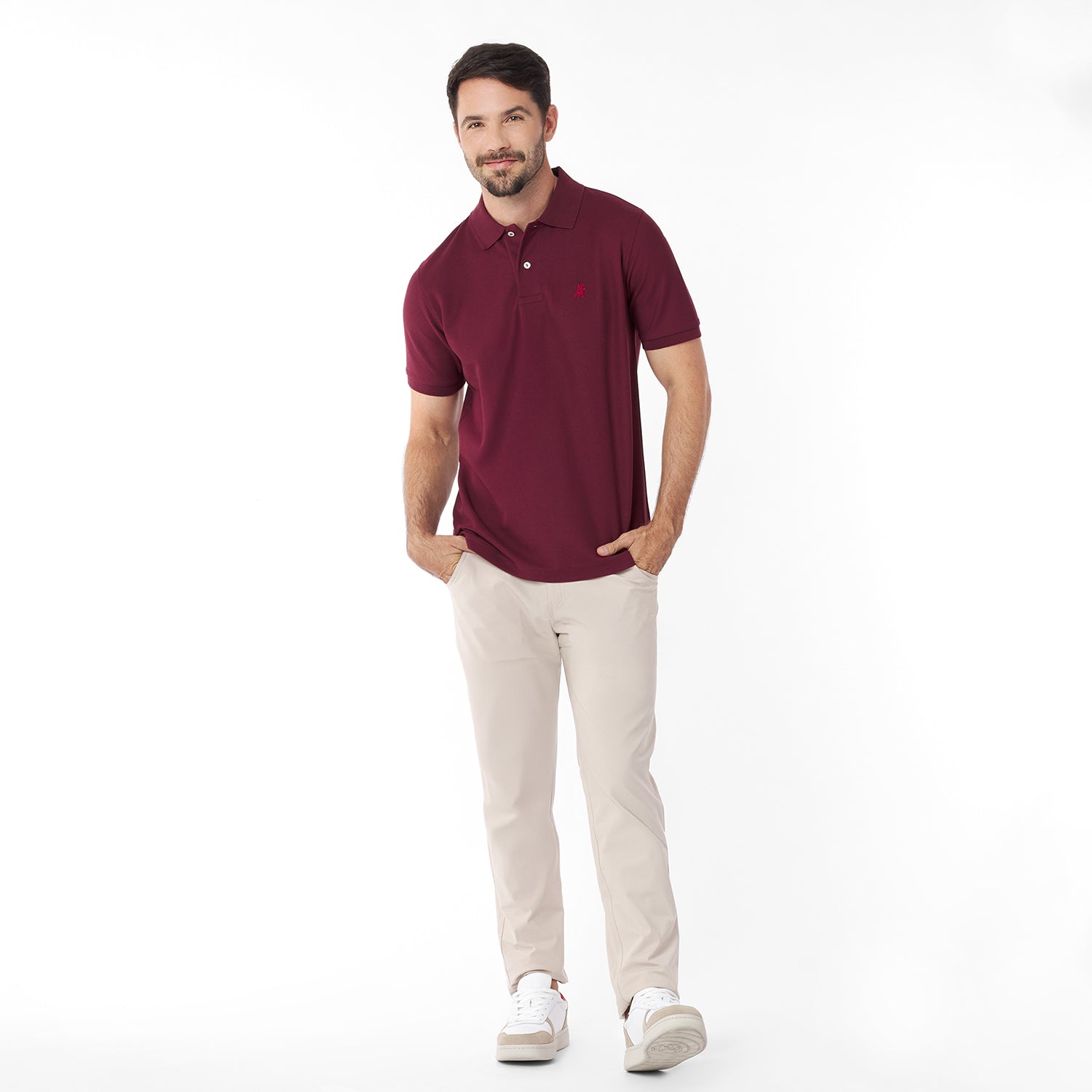 Man wearing a maroon polo shirt and beige pants on a white background
