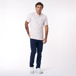 Man wearing a light pink polo shirt with navy pants on a white background
