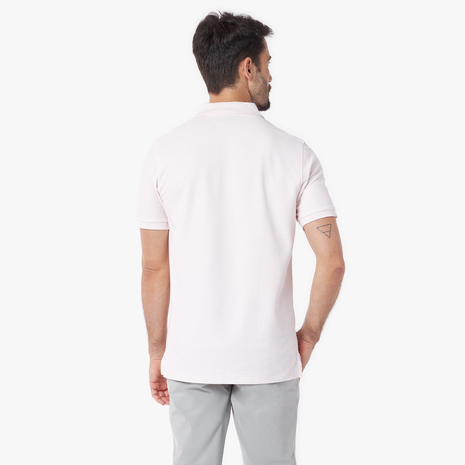 Back view of a man wearing a light pink polo shirt and light gray pants on a white background