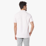 Back view of a man wearing a light pink polo shirt and light gray pants on a white background