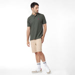 Full body view of a man wearing a green polo shirt with a red logo