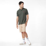 Full body view of a man wearing a green polo shirt with a red logo