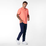 Man wearing a coral polo shirt and navy pants on a white background