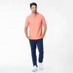 Man wearing a coral polo shirt and navy pants on a white background
