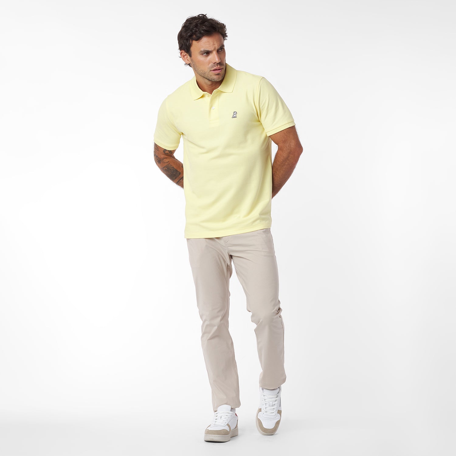 Man wearing a light yellow polo shirt and beige pants on a white background