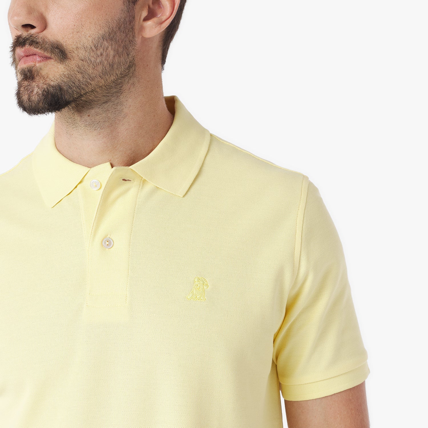 Close-up of a man wearing a light yellow polo shirt with a small logo on a white background