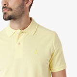 Close-up of a man wearing a light yellow polo shirt with a small logo on a white background