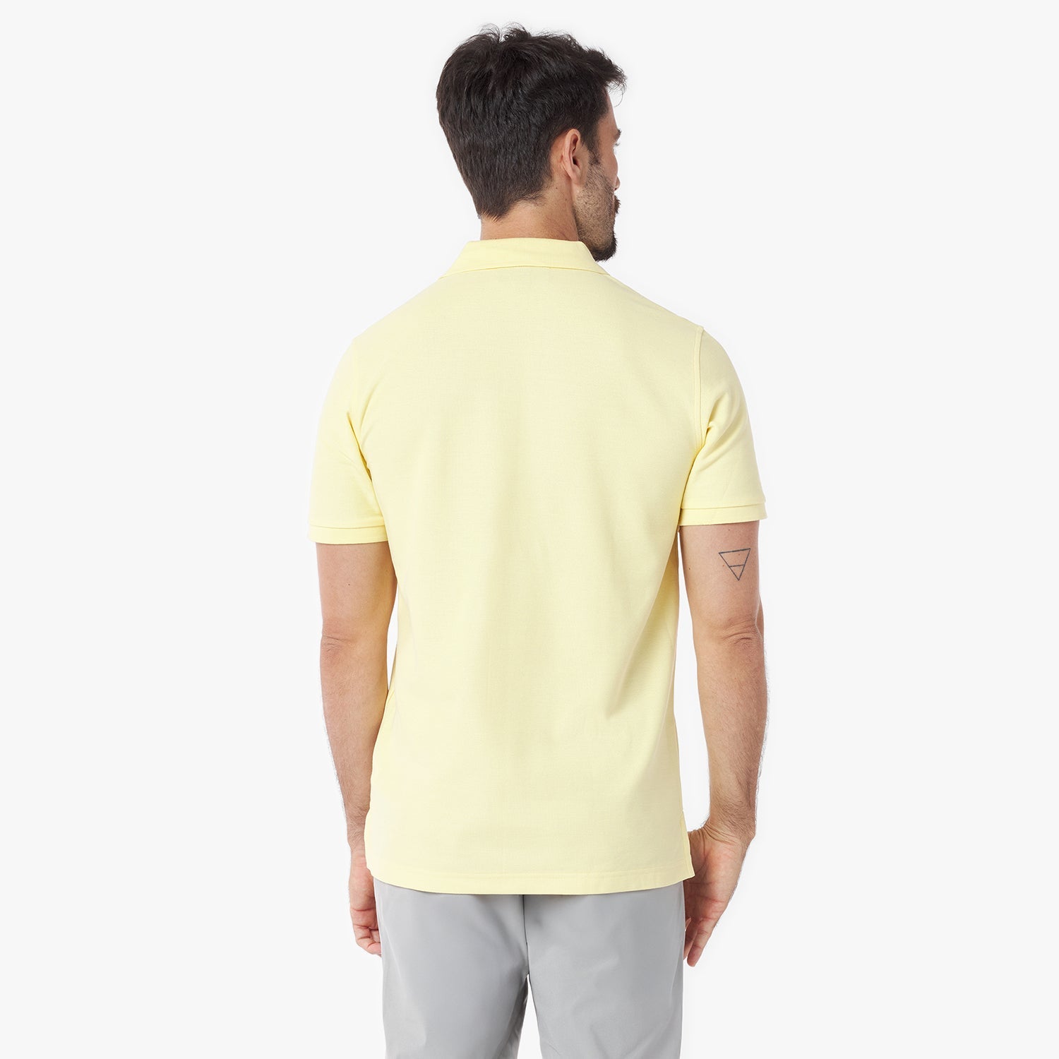 Back view of a man wearing a light yellow polo shirt on a white background