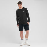 Man wearing a black long-sleeve shirt and shorts with white sneakers on a light gray background