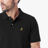 A close-up of a man wearing a black short-sleeve polo shirt with a small gold embroidered dog logo on the left chest