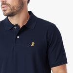 A close-up of a man wearing a navy blue polo shirt with a small embroidered dog logo on the left chest