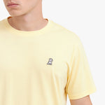 Close-up of a yellow t-shirt with a small logo on a white background