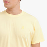 Close-up of a yellow t-shirt with a small logo on a white background
