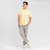 Man wearing a yellow t-shirt and gray pants on a white background