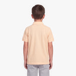 A child viewed from the back wearing a short-sleeve polo shirt in a pale peach-beige color, paired with light gray pants, against a plain white background.