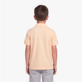 A child viewed from the back wearing a short-sleeve polo shirt in a pale peach-beige color, paired with light gray pants, against a plain white background.