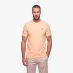 Man wearing a beige t-shirt with a small logo on a white background