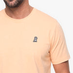 Close-up of a man wearing a peach color t-shirt with a white embroidered dog logo