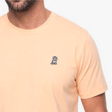 Close-up of a man wearing a peach color t-shirt with a white embroidered dog logo