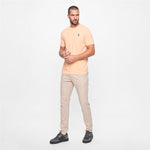 A man wearing a peach color t-shirt with beige pants on a white background