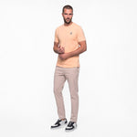 Man wearing a peach t-shirt and beige pants on a white background