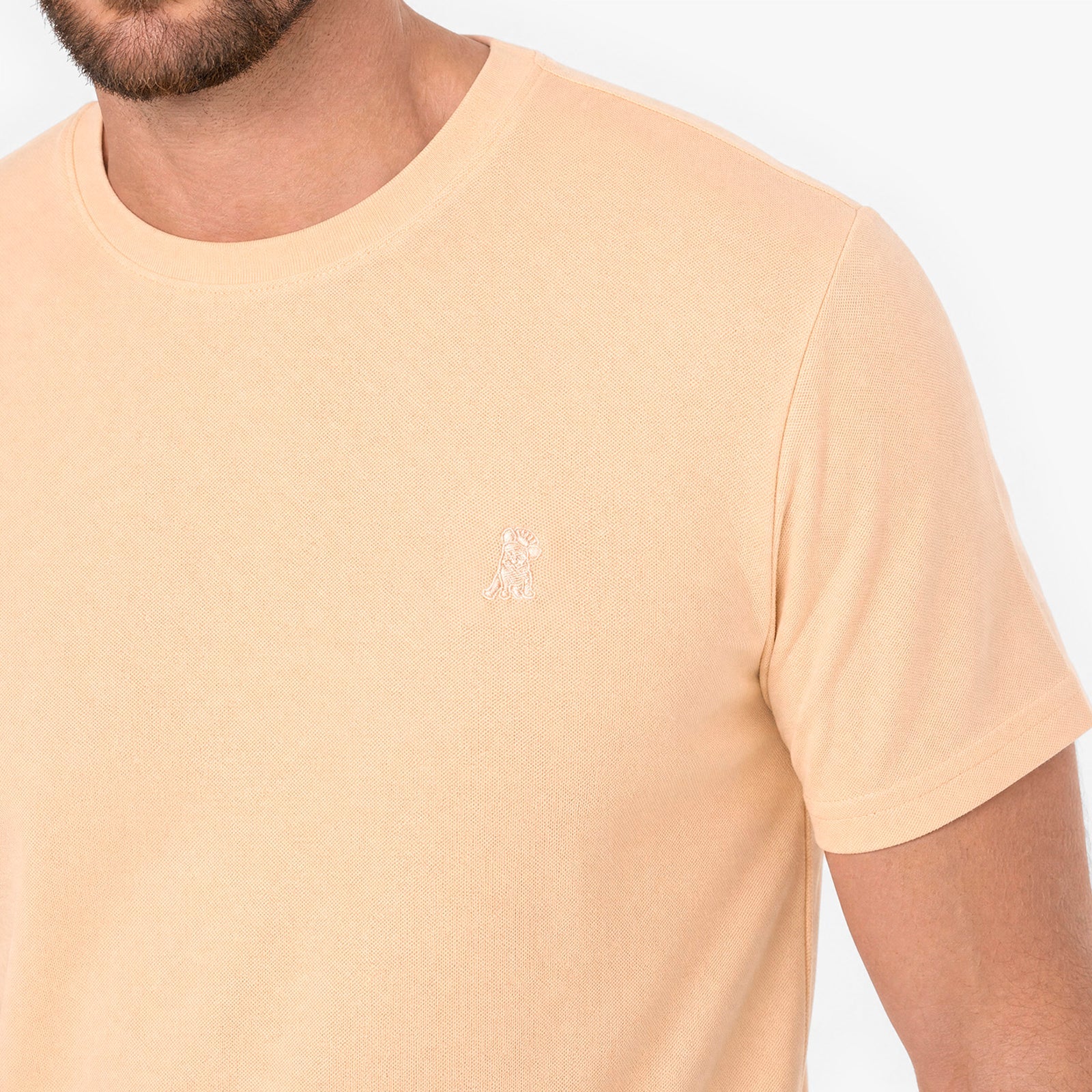 Beige t-shirt with a small logo on a plain background