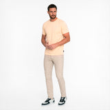 A man wearing a peach T-Shirt with beige pants on a white background