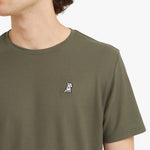 Close-up of a man wearing a green t-shirt with a small logo on the chest against a plain background