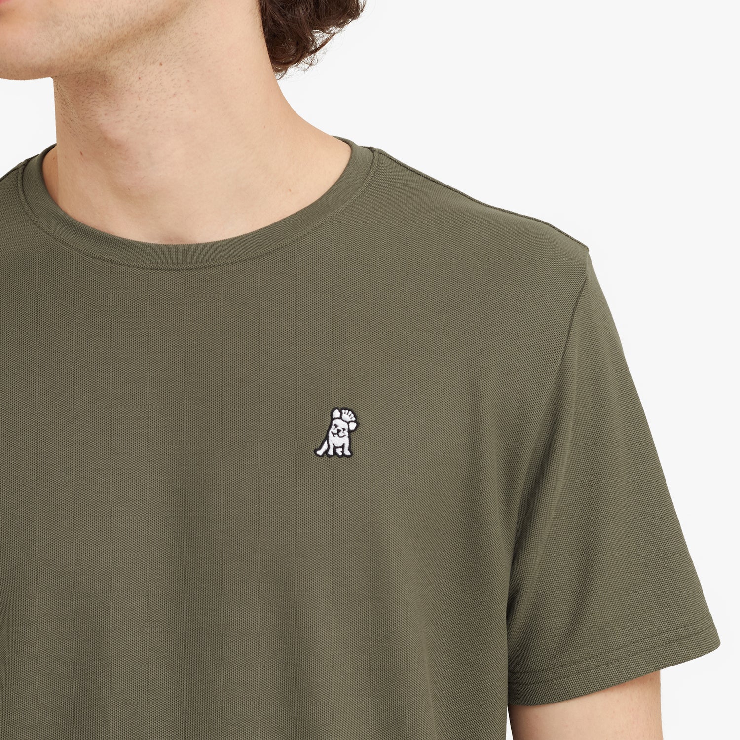 Close-up of a man wearing a green t-shirt with a small logo on the chest against a plain background