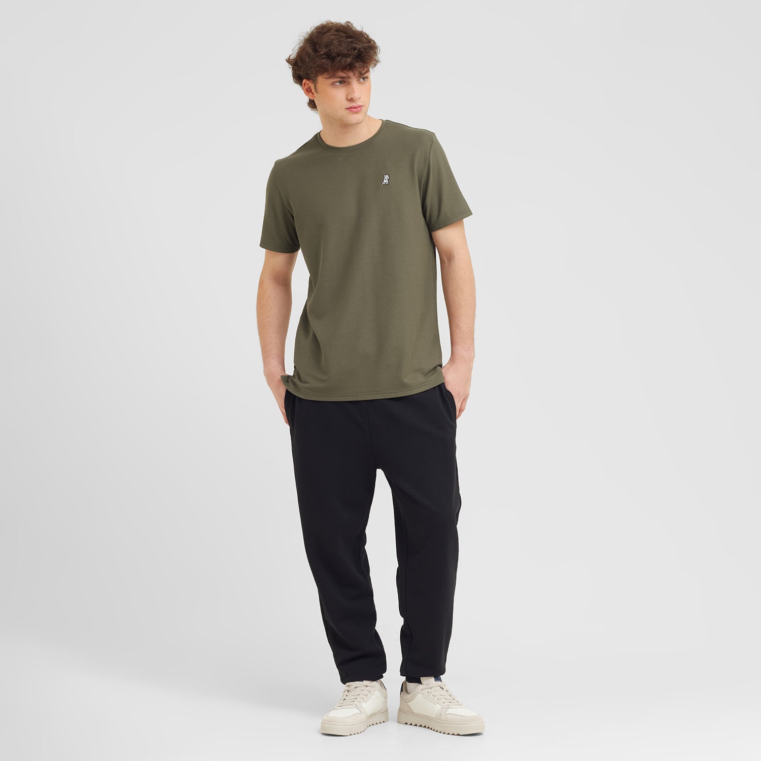Man wearing an olive green t-shirt and black pants on a white background