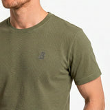 Close-up of a person wearing a green t-shirt with a small logo on a light gray background