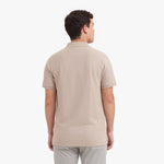 Back view of a man wearing a beige polo shirt on a white background