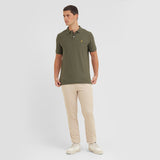 Man wearing a green polo shirt and beige pants on a white background