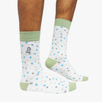 White socks with blue and green patterns and green accents worn by a person on a white background