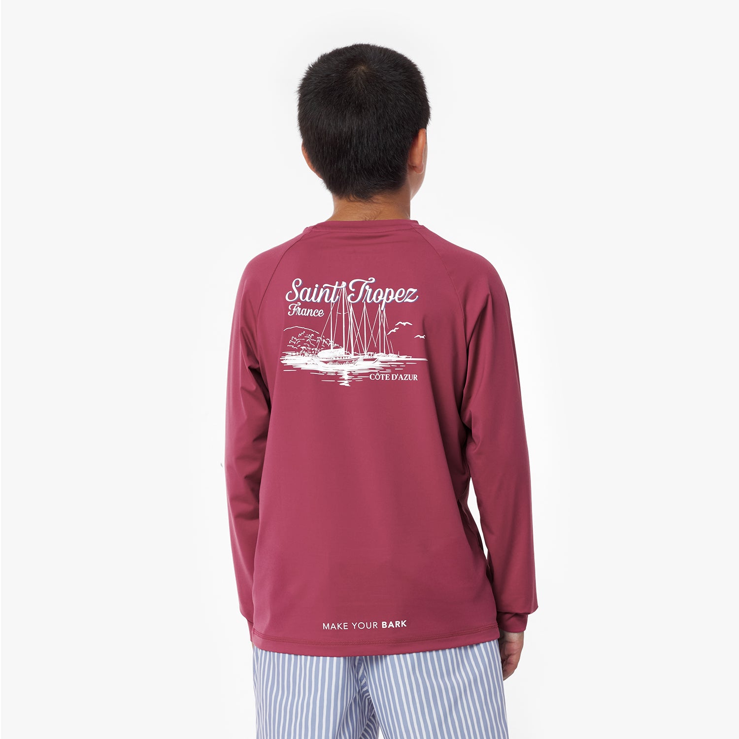 Boy wearing a maroon rashguard with 'Saint Tropez' print on the back